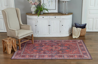 Beige upholstered wingback chair with nailhead trim, wooden stump side table, red Persian rug, white distressed curved cabinet.