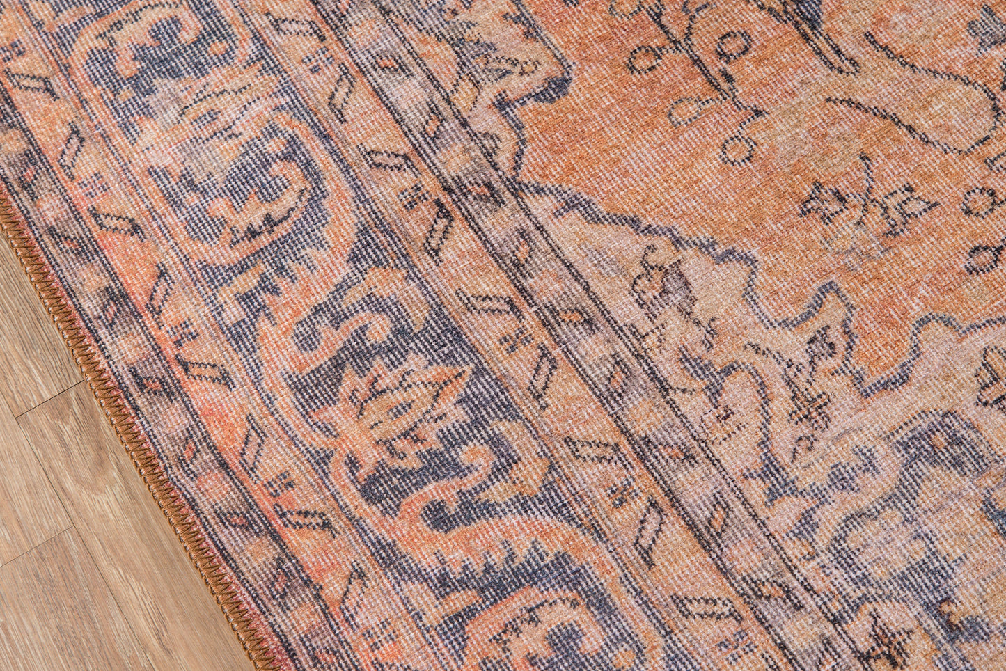 Close-up of orange & blue Persian-style rug with floral motifs and fringe along the edge on wood floor.