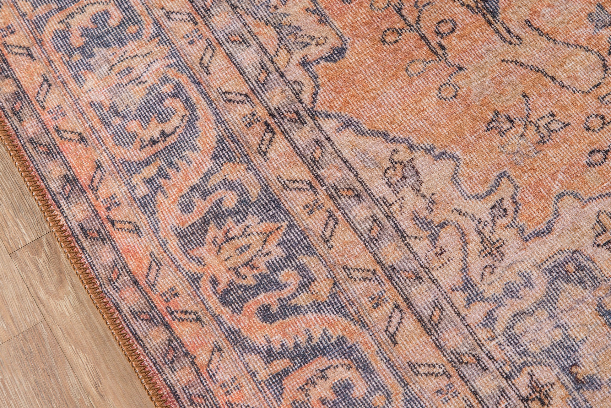 Orange and blue traditional Oriental rug with floral medallion pattern and fringed edge on a wood floor.