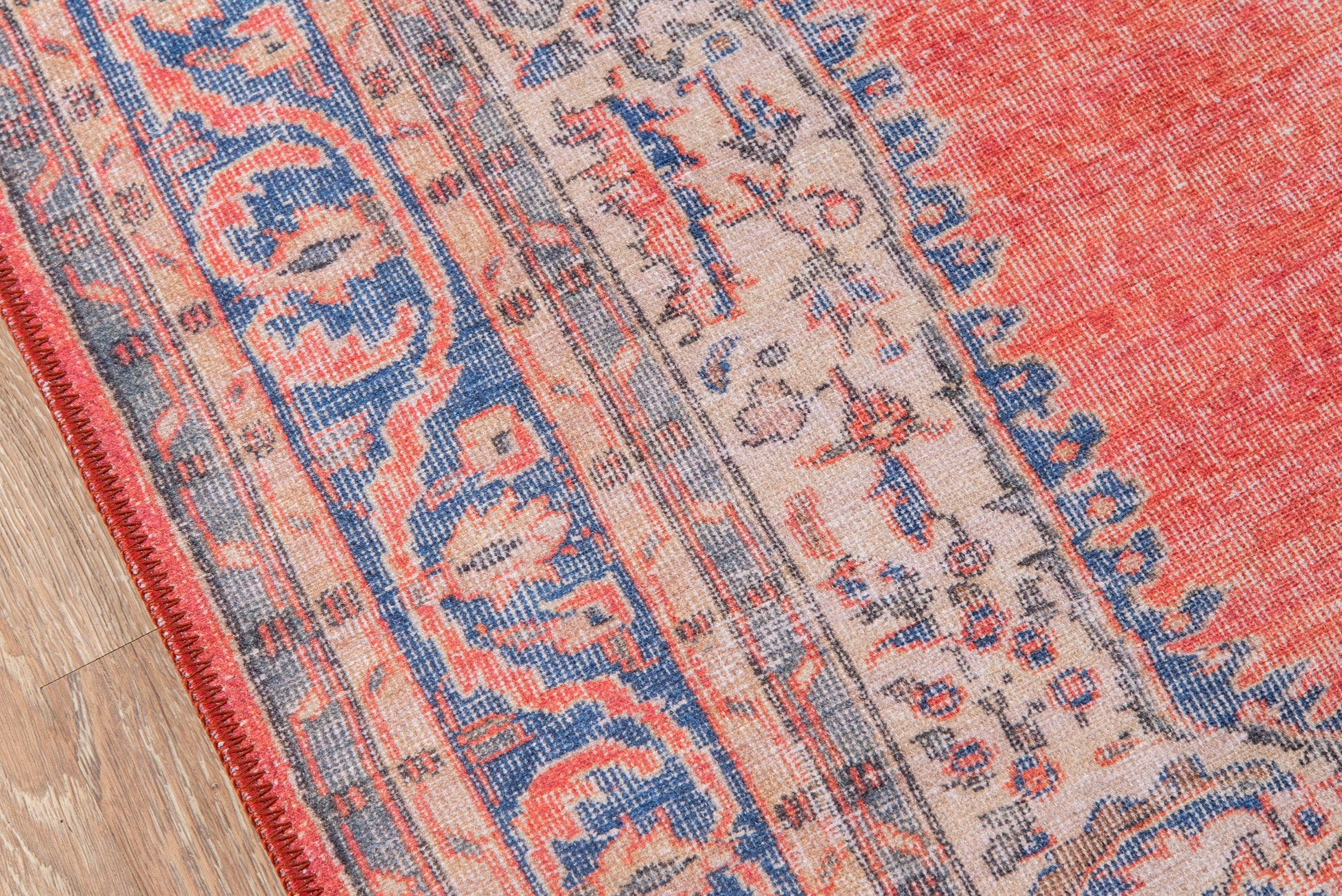 Rectangular red and blue oriental rug with beige central field, floral motifs and decorative borders on a wooden floor.