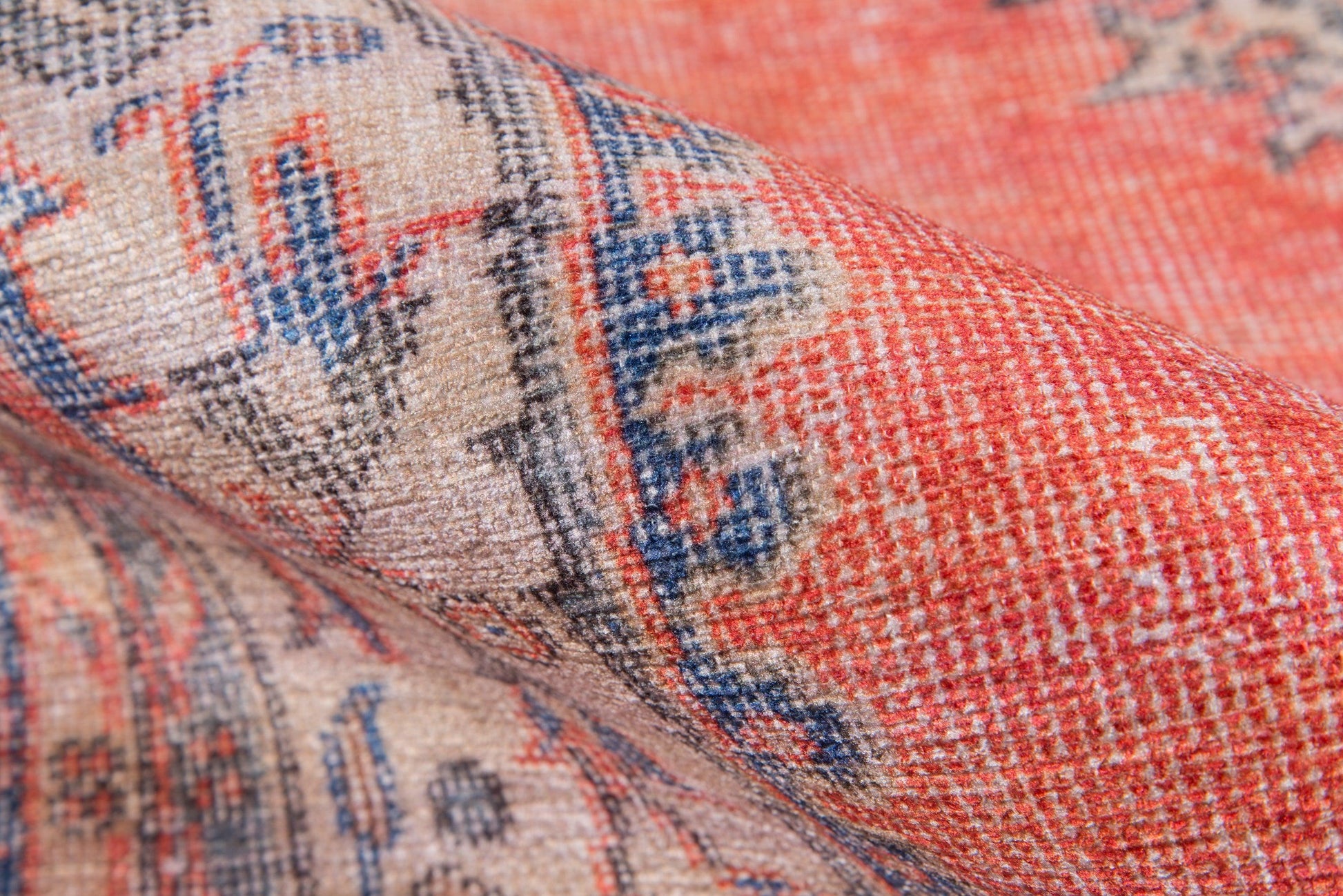 Close-up of red, cream and blue woven rug with geometric oriental pattern and folded edge.