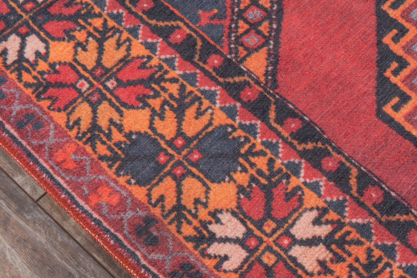 Red oriental rug with orange and navy geometric floral pattern and decorative border on wood floor