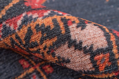 Rolled woven oriental rug with red, orange, black and beige geometric motifs.