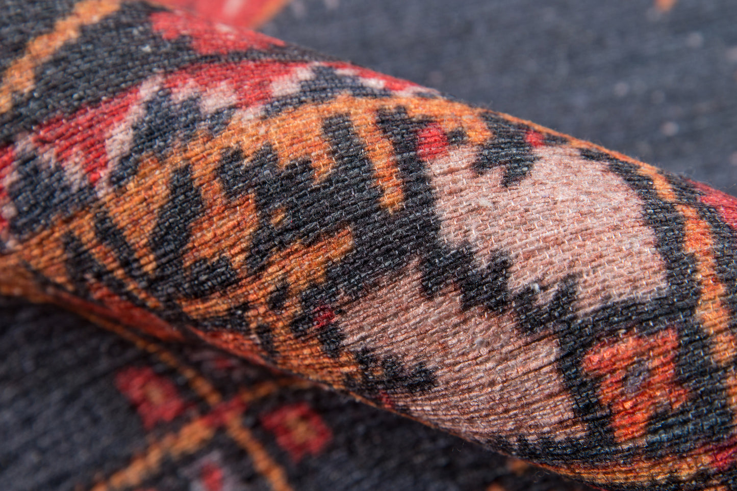 Rolled oriental wool rug with geometric tribal pattern in red, orange, black and tan.