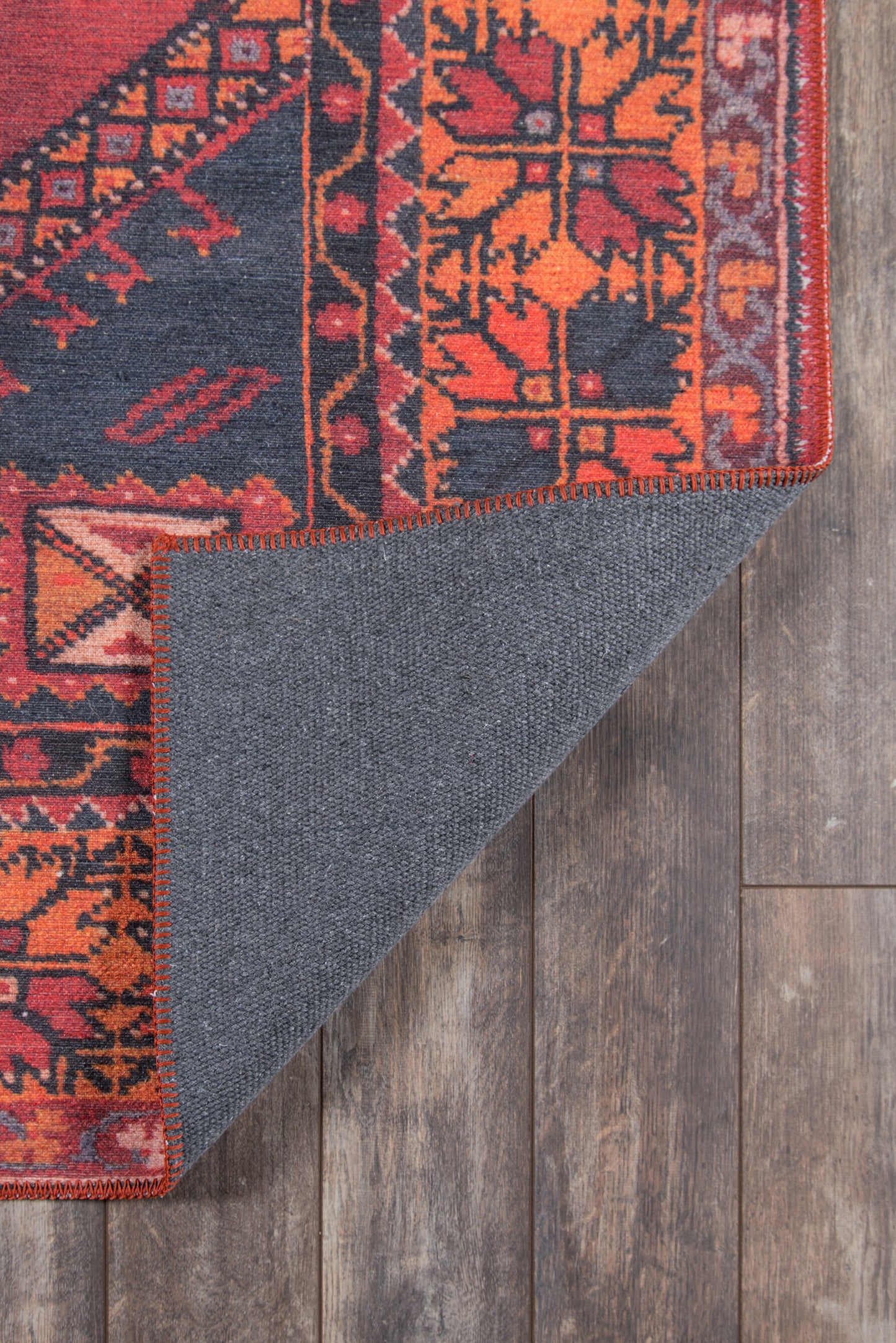 Colorful oriental rug with red/orange floral pattern and navy field; folded corner reveals blue underside and red stitch.
