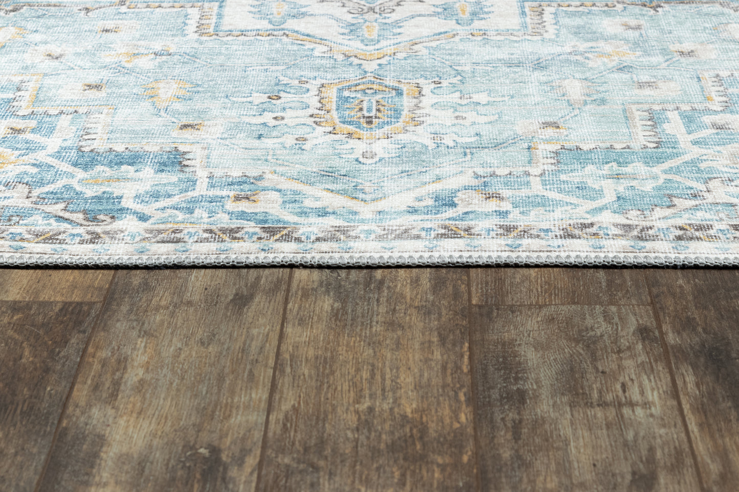 Turquoise and white ornate area rug with fringe edge on dark wood floor