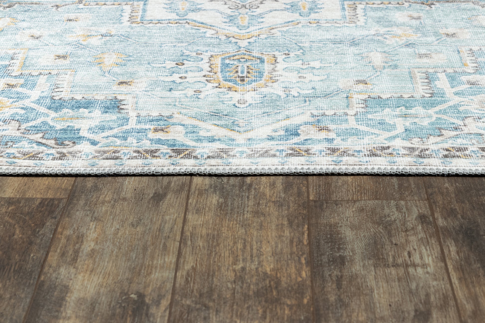 Blue patterned area rug with light blue and white geometric design on dark wood floor; fringe along edge.
