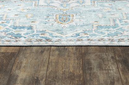 Blue patterned area rug with light blue and white geometric design on dark wood floor; fringe along edge.