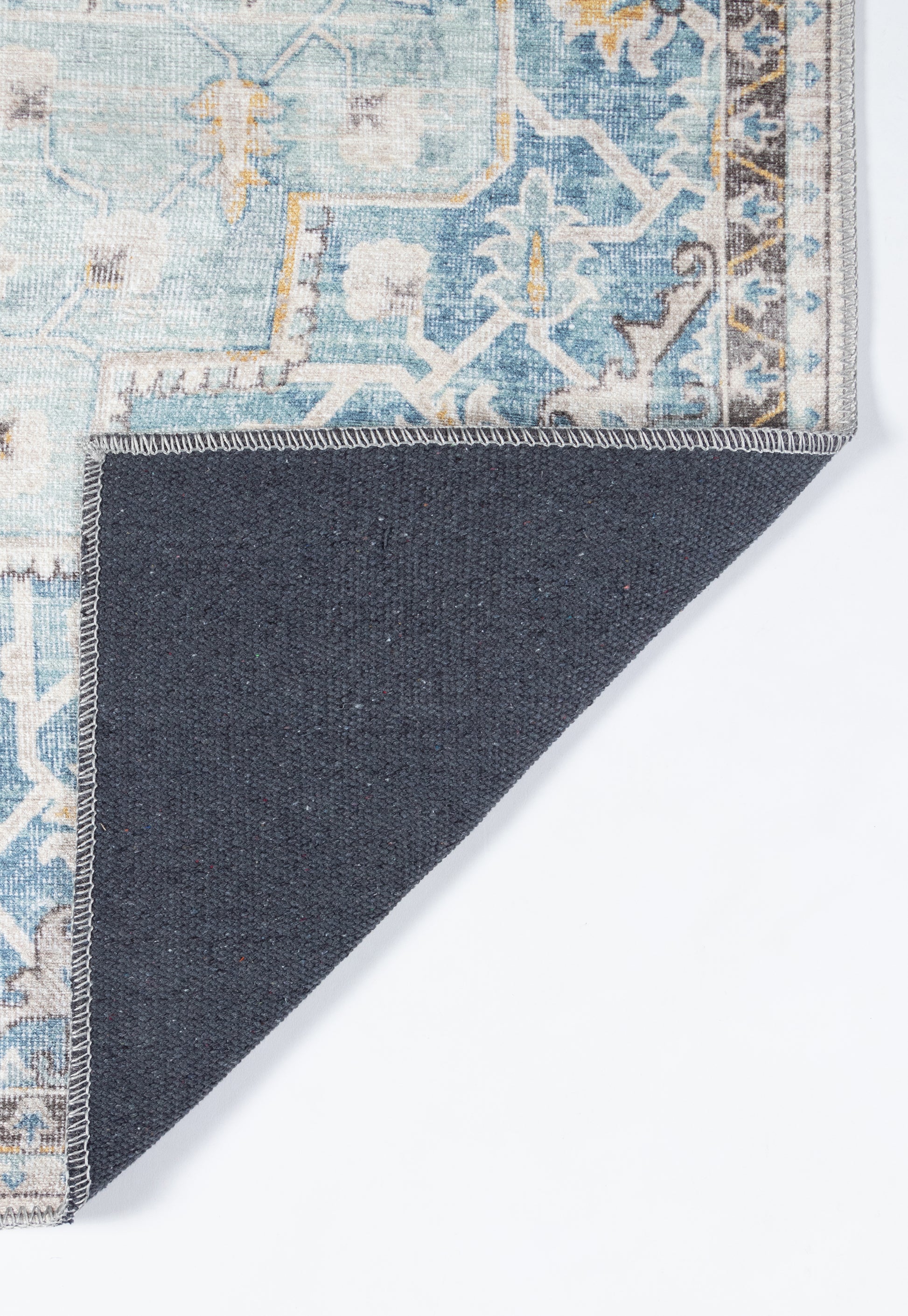 Blue patterned rug with faded floral-geometric design and light border; corner folded to reveal dark navy backing.