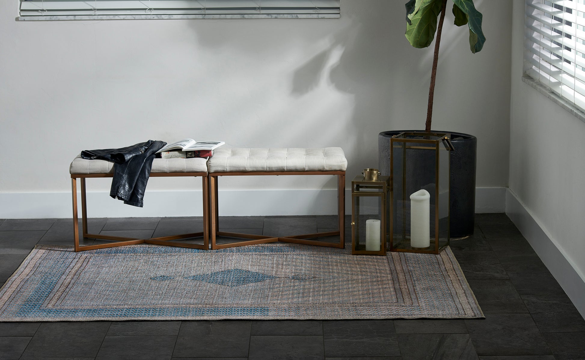 Blue-gray patterned rug in a living area with metal lanterns and a black planter holding a tall plant.