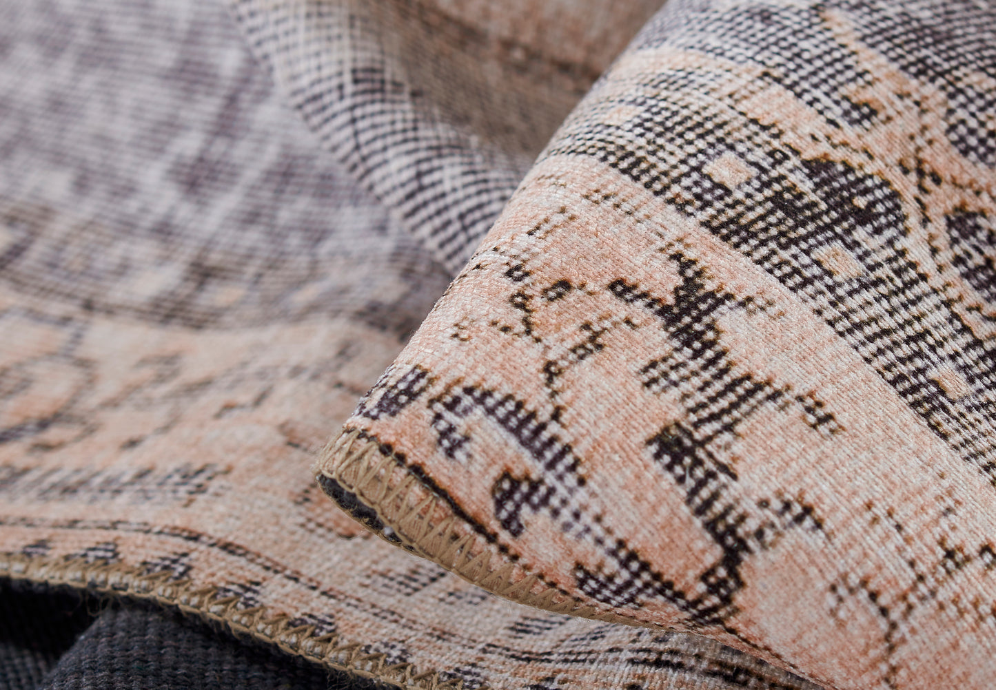 Close-up of woven rug fabric in peach, beige and black with geometric pattern, textured weave and visible fringe.