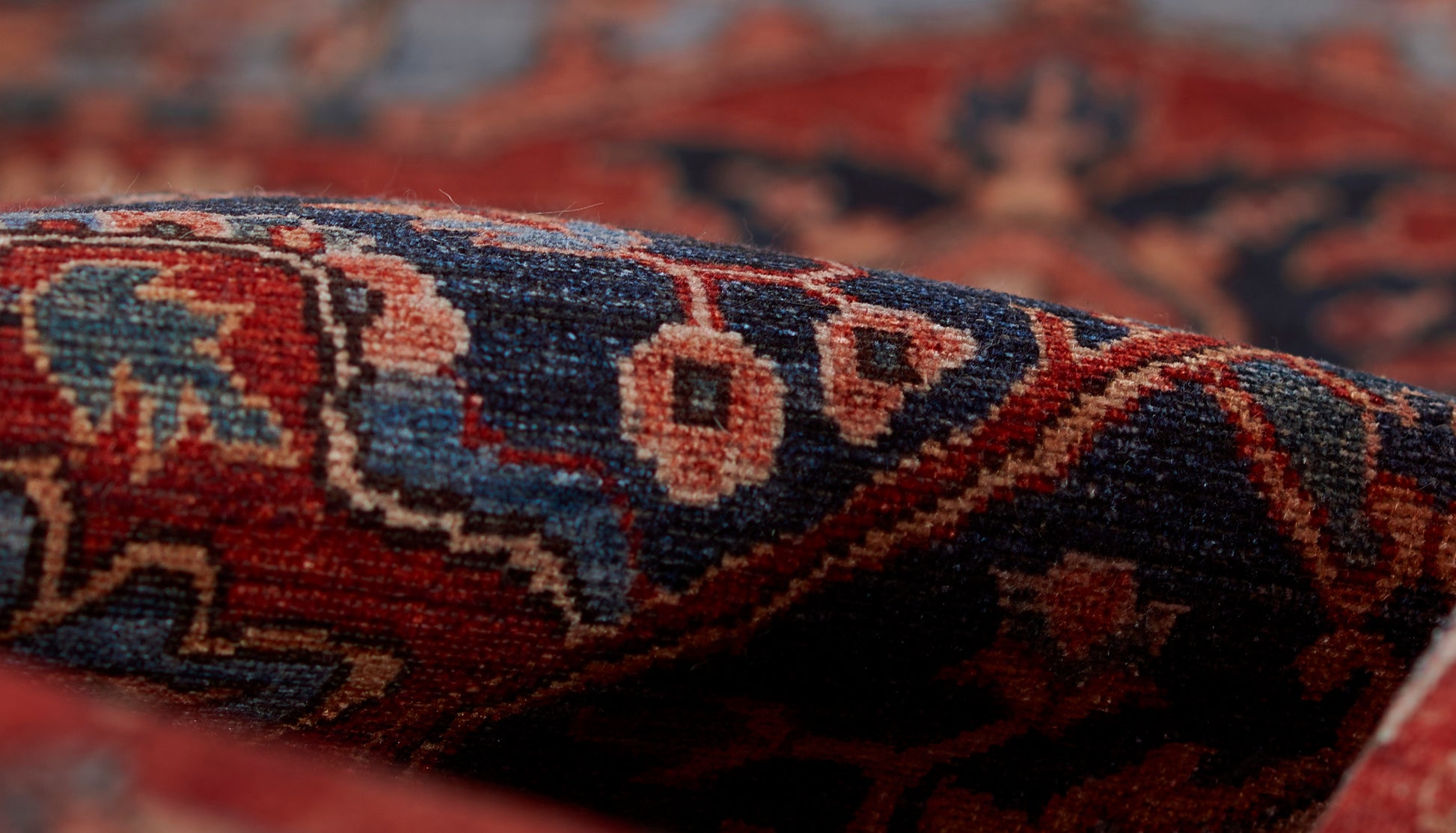 Close-up of a woven rug with red, blue and ivory geometric motifs and rich texture.