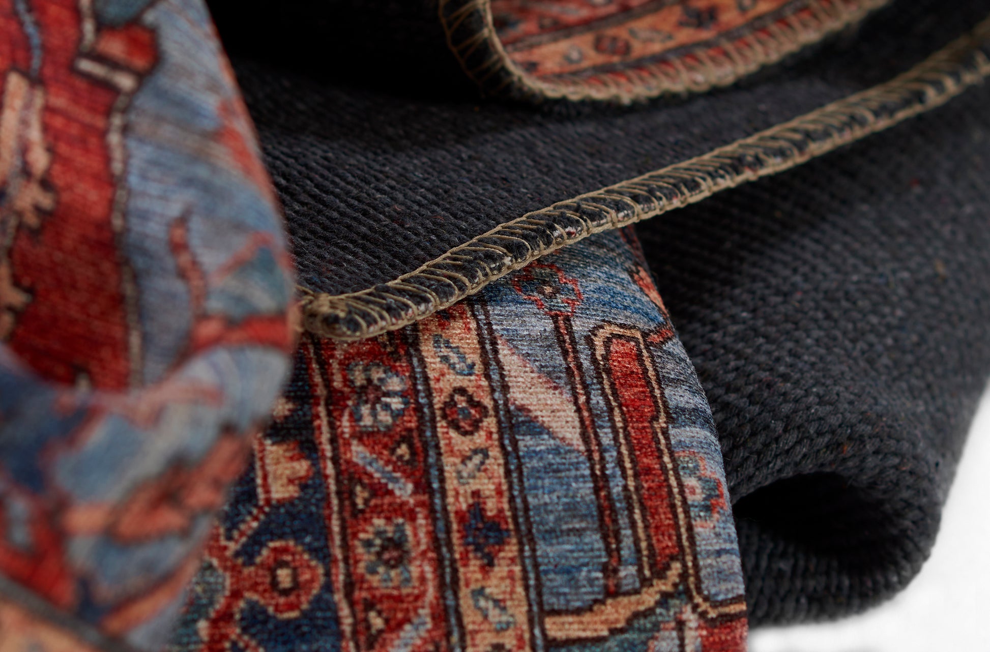 Close-up of a colorful woven rug with red, blue & beige geometric motifs and folded edge.