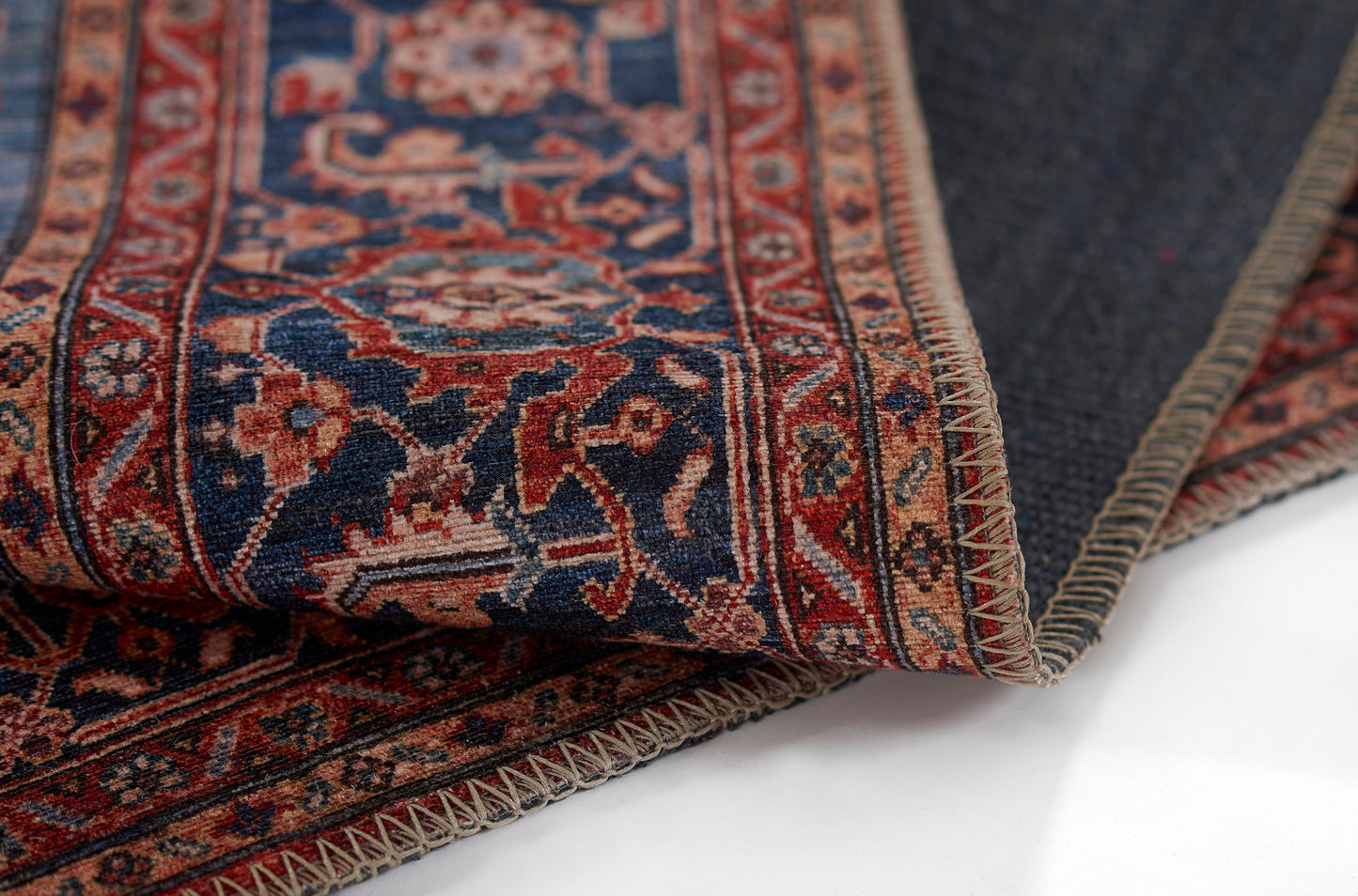 Persian-style runner rug, 2' x 8', in red and navy with cream floral motifs, folded to reveal its woven fringe edge.