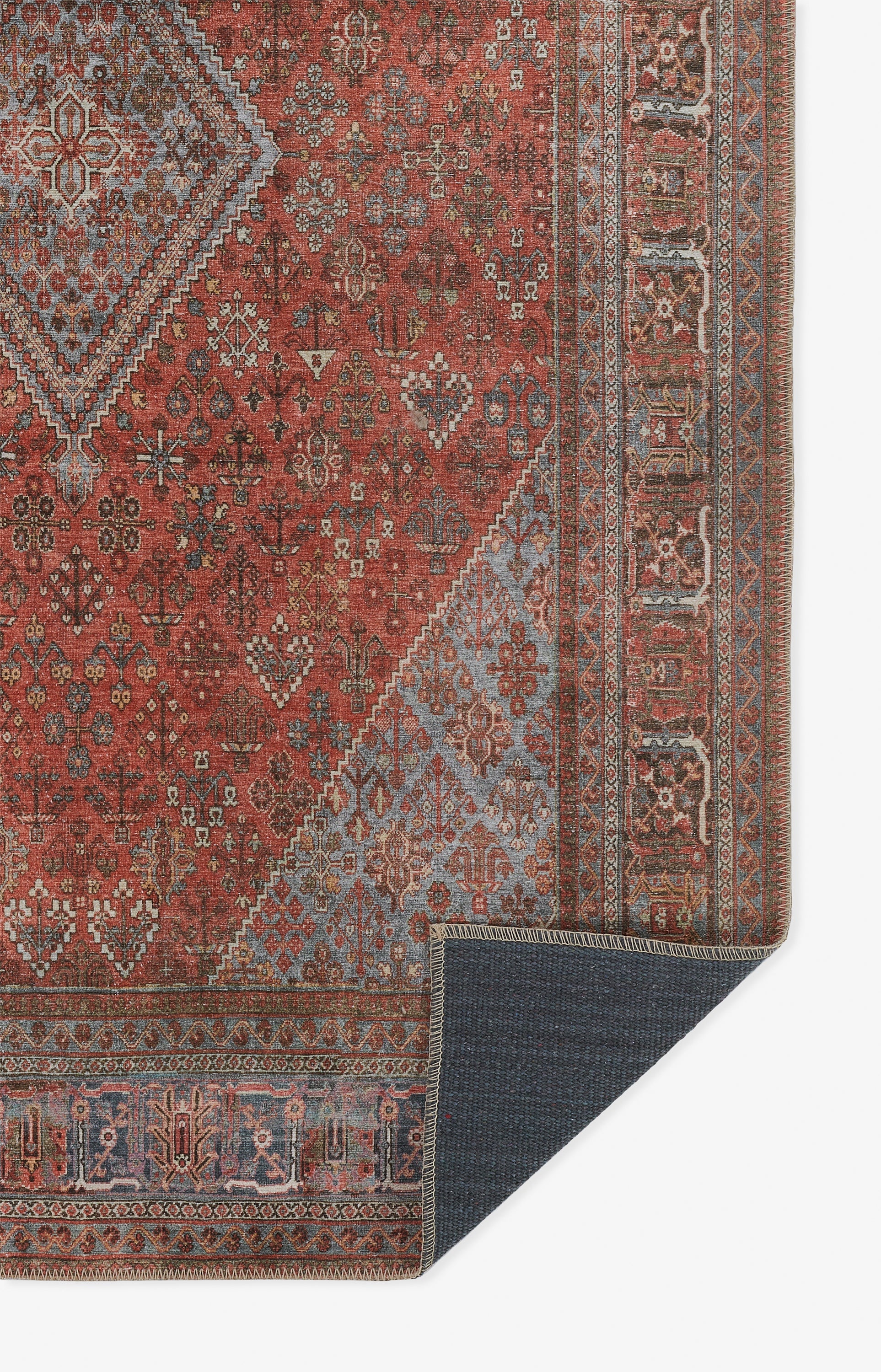Red oriental rug with blue floral motifs and beige borders; corner fold shows dark-blue underside.