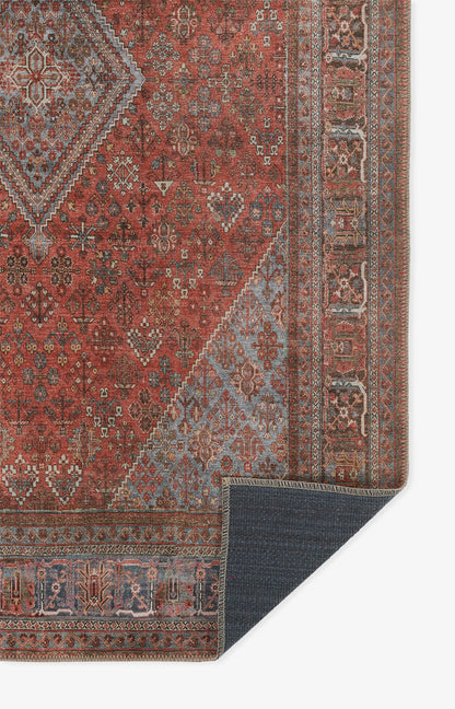 Red oriental rug with blue floral motifs and beige borders; corner fold shows dark-blue underside.
