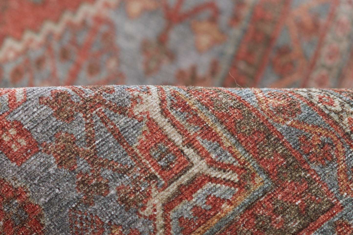 Close-up of a woven rug with red, rust, blue and beige geometric motifs; textured wool.