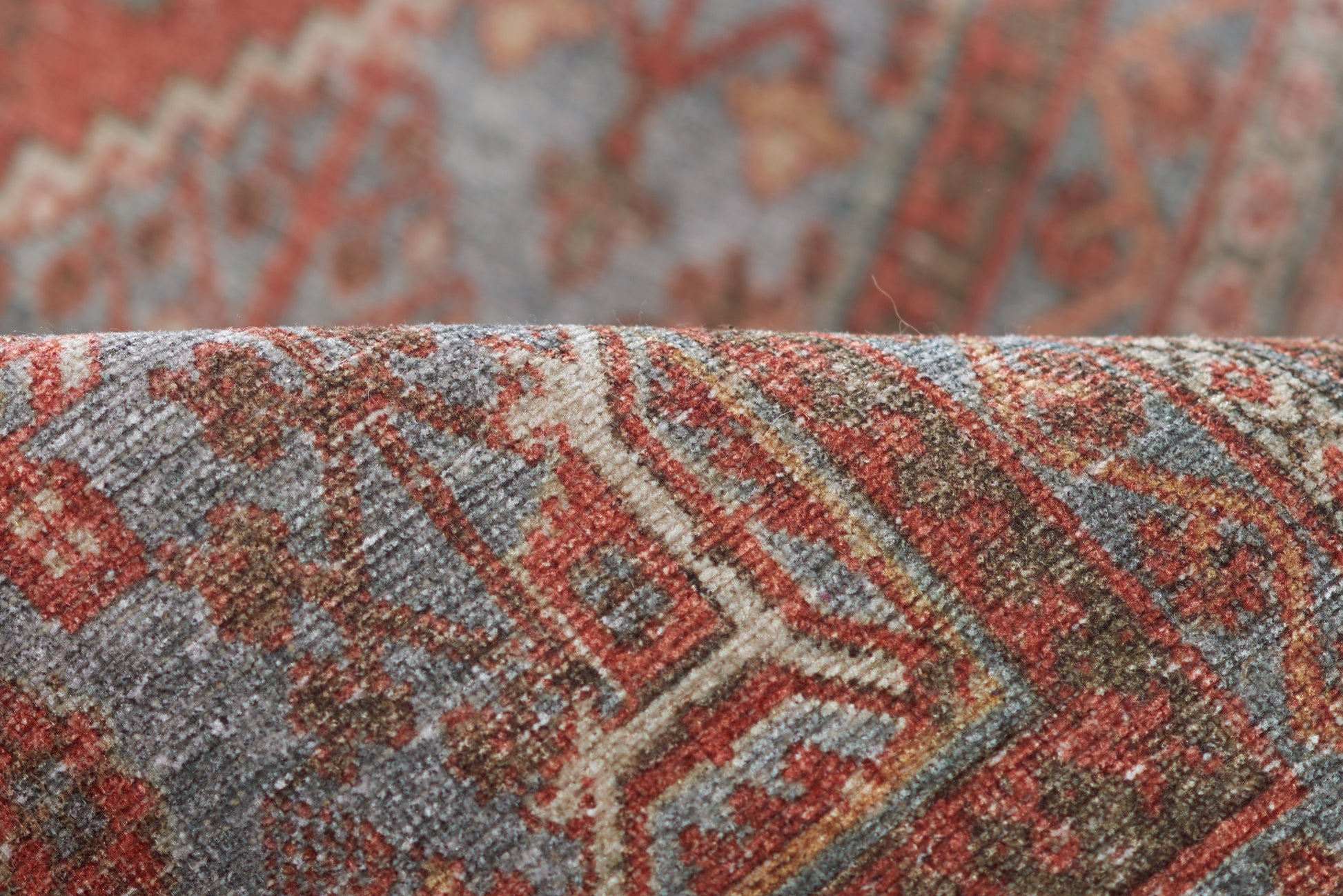 Close-up of a woven rug with red, rust, blue and beige geometric motifs; textured wool.