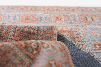 Close-up of a traditional Persian rug in blue, red and beige hues, woven wool with a fringed edge.