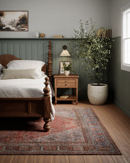Persian rug on the floor in a bedroom scene, with a traditional wooden four-poster bed, white linens, nightstand, sage paneling, and a large potted tree.