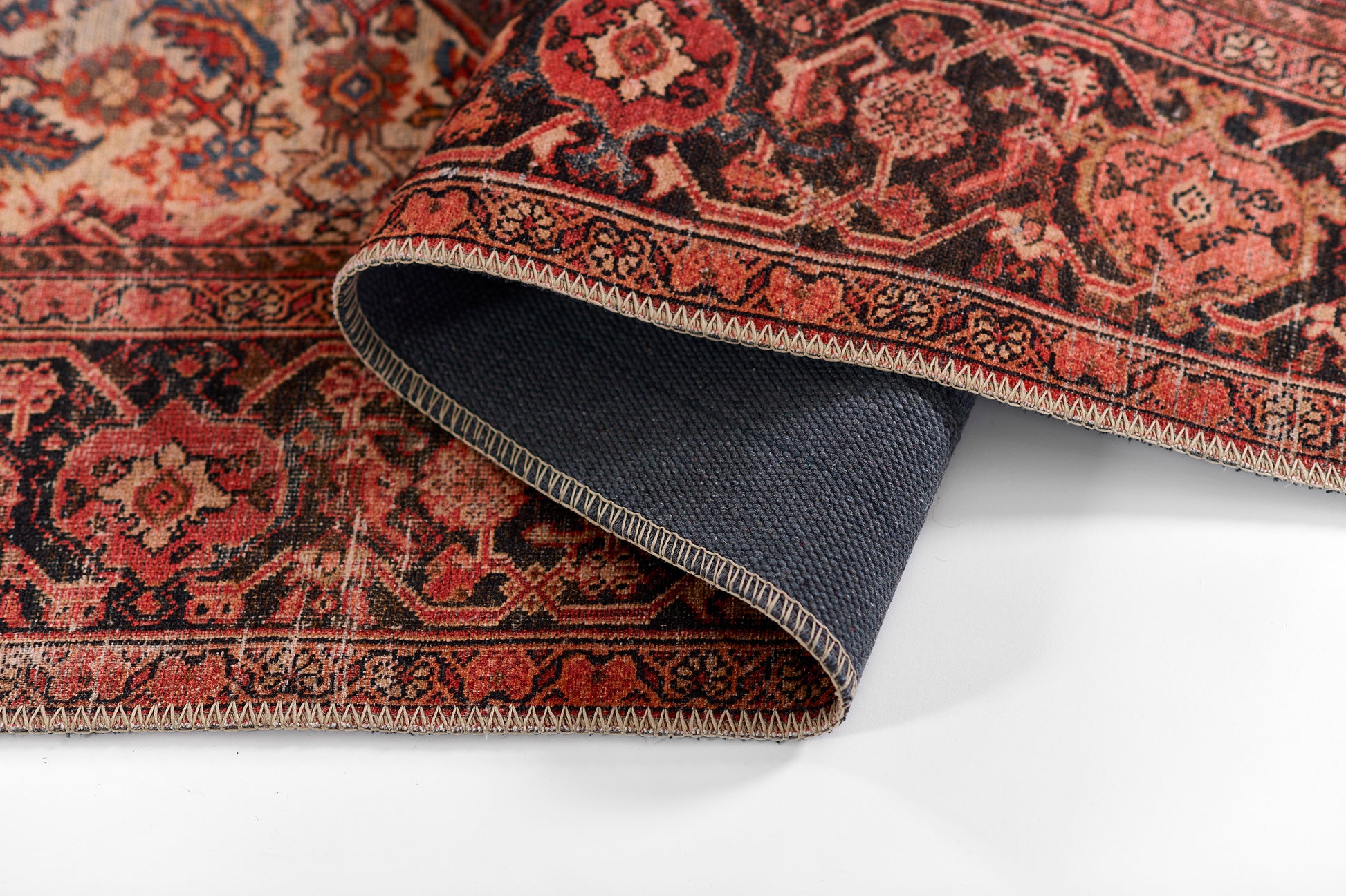 Red Persian-style rug with ornate floral pattern and border, partially folded to reveal blue backing.