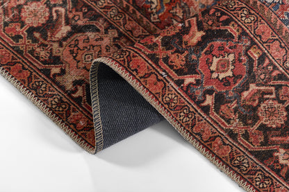 Red Persian-style rug with intricate floral motifs; folded corner reveals navy underside and zigzag stitched edge