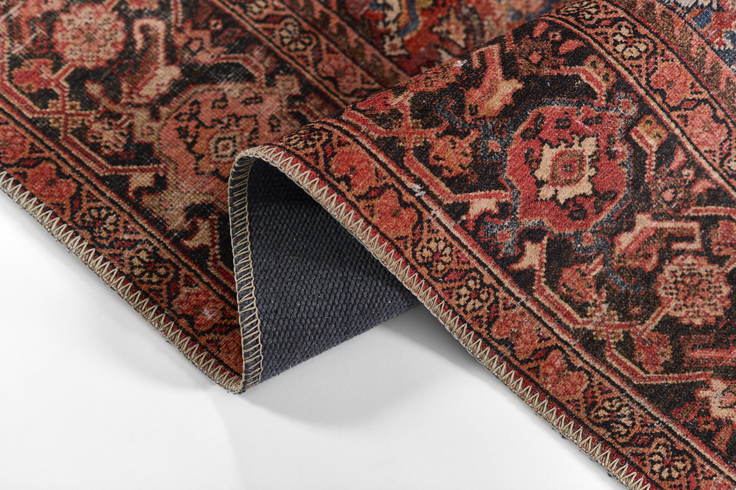 Red oriental rug with floral motifs, folded to show navy blue backing and white zigzag edge stitching.