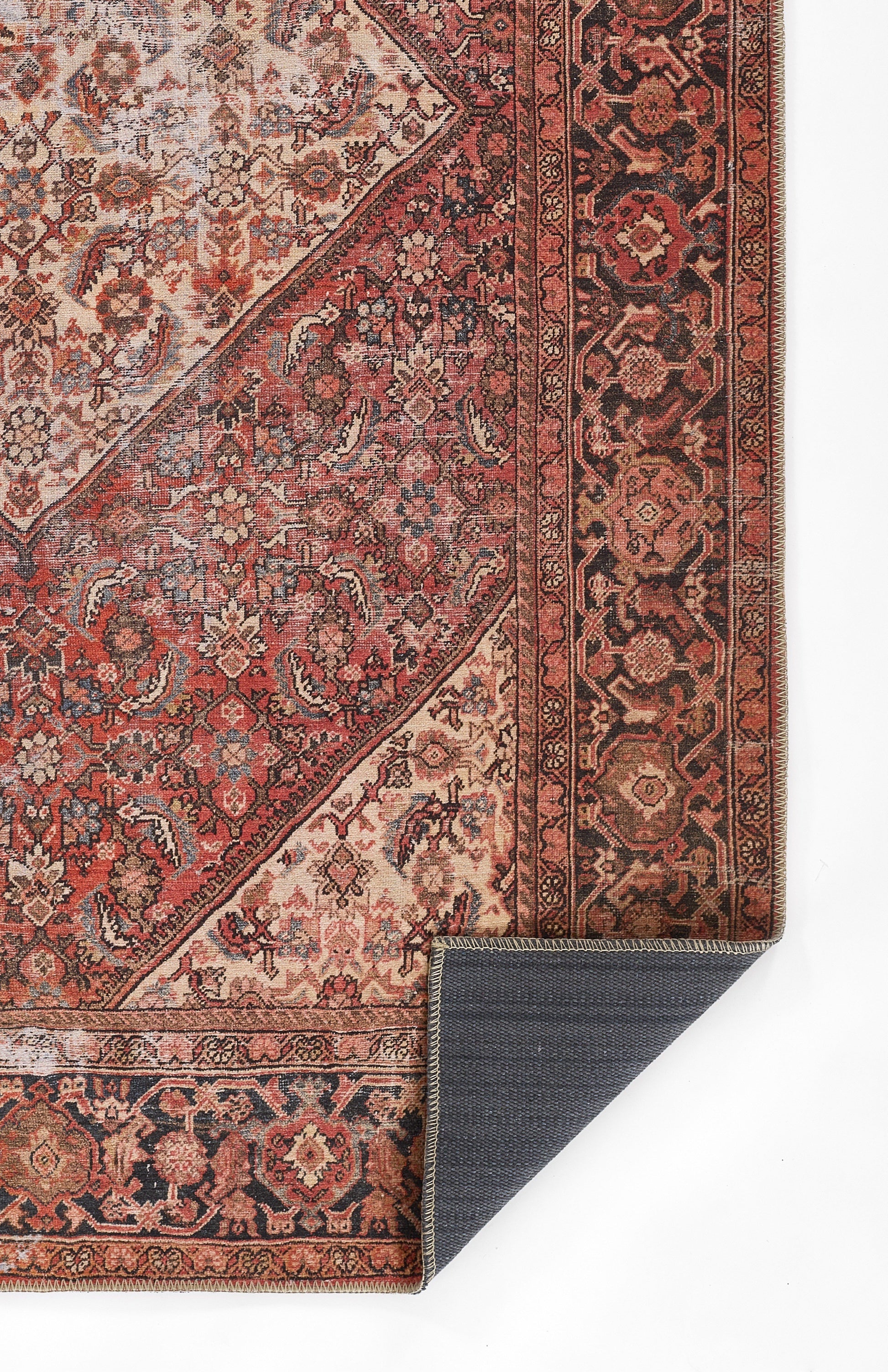 Persian-style red oriental rug with intricate floral patterns and dark bordered edges; corner folded to show navy back.
