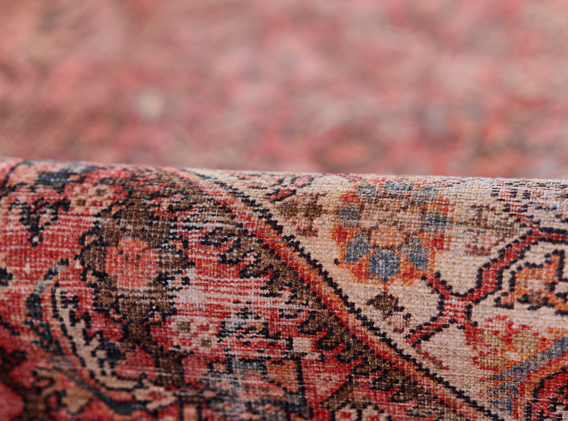 Close-up of a red Persian-style rug with floral motifs, woven wool, folded edge, warm beige, blue and black accents.