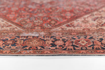 Close-up of a red Persian-style rug with a navy blue border & floral motifs; woven pile & fringe edge.
