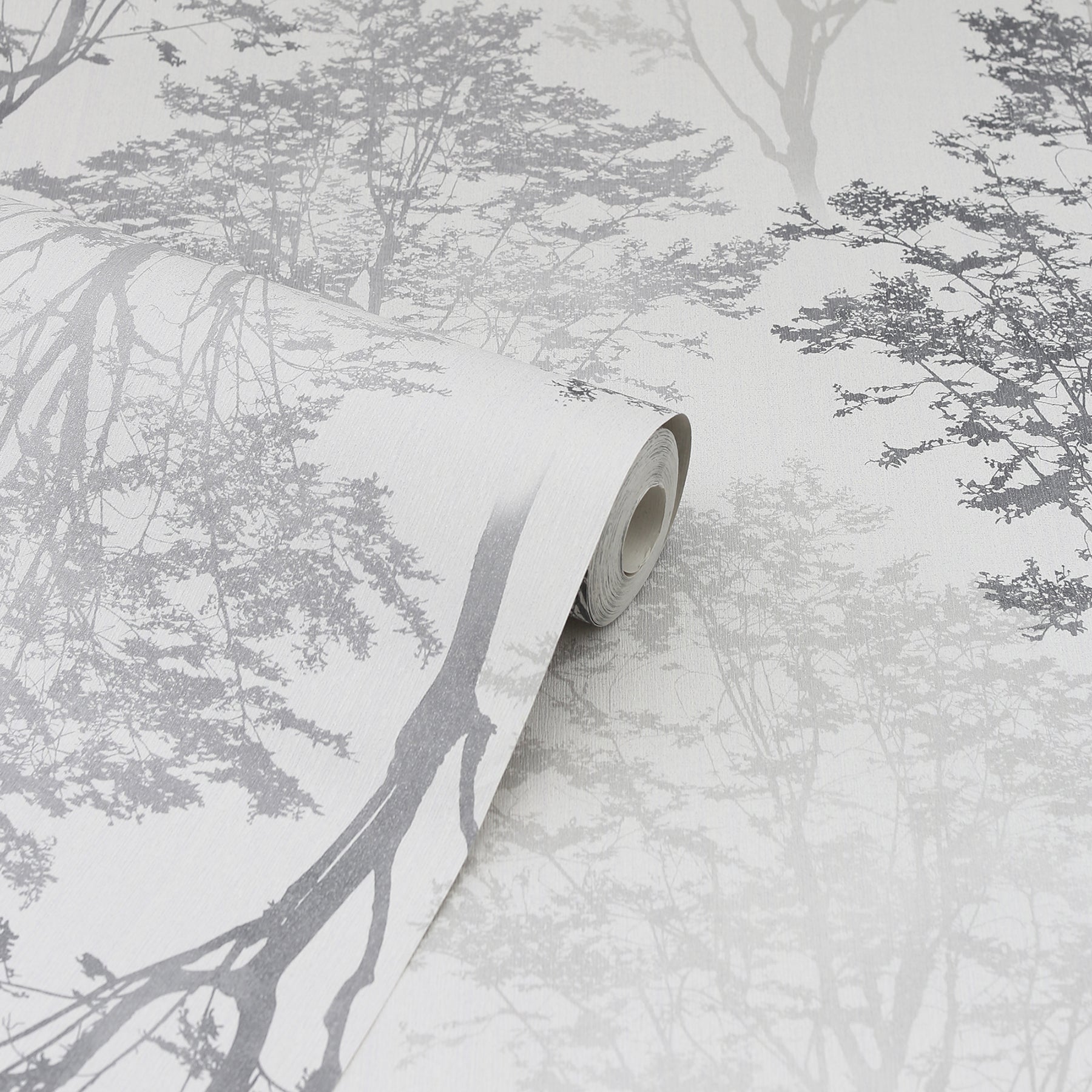 Gray-scale forest/tree branch wallpaper roll with rolled edge on a pale background; decorative wallcovering
