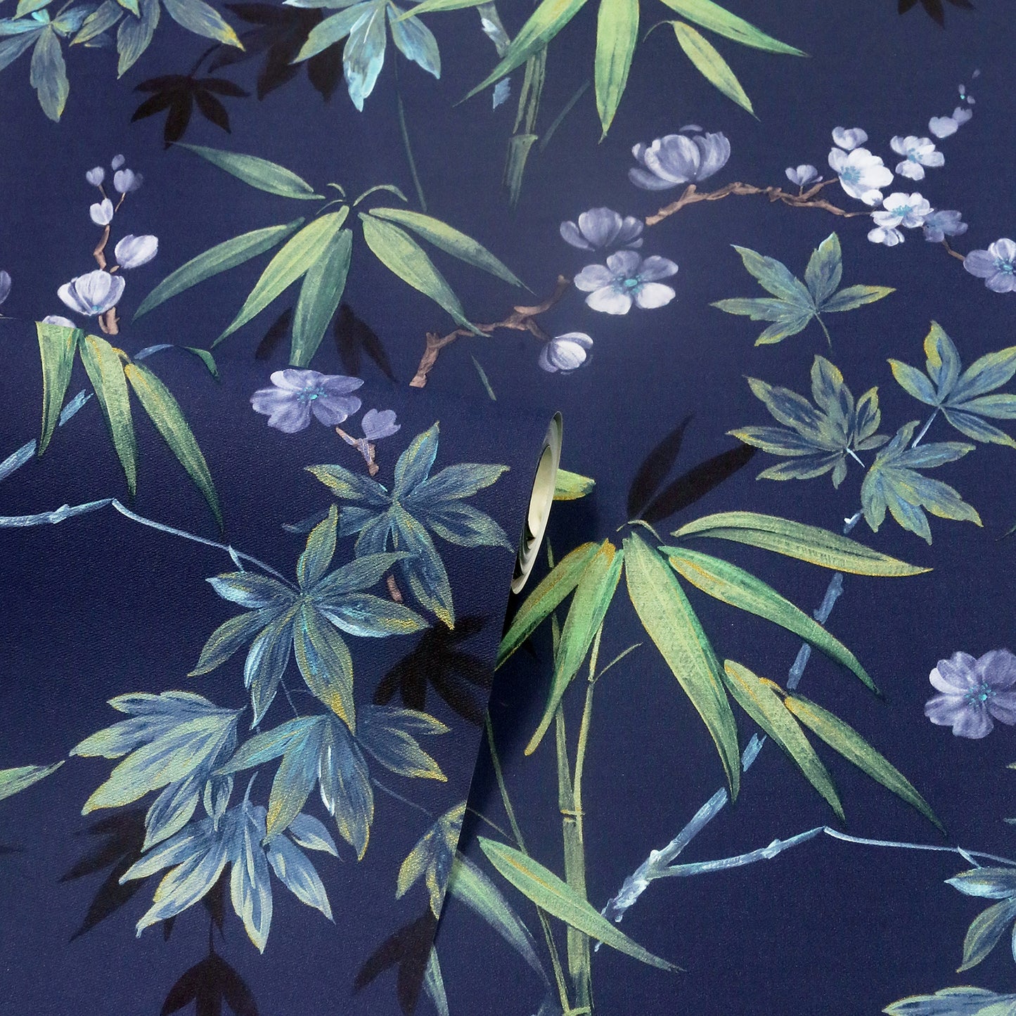 Navy blue fabric with bamboo leaves and pale purple flowers in green/teal tones; folded edge visible, botanical print.