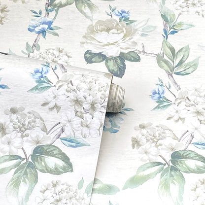 Wallpaper roll with watercolor floral design: white roses, blue blossoms & green leaves on a light cream background.