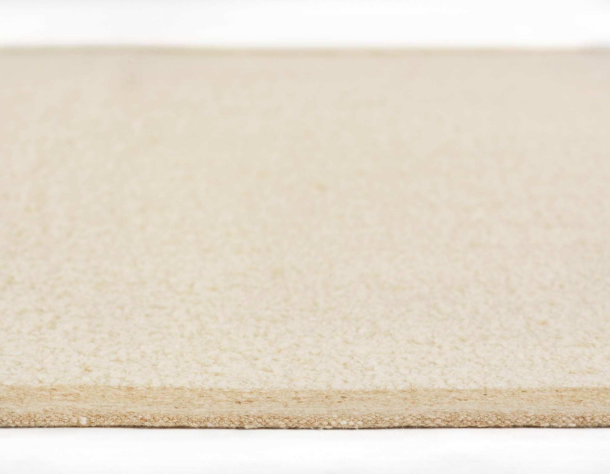 Close-up of a light beige rug showing a smooth woven texture and rectangular shape.