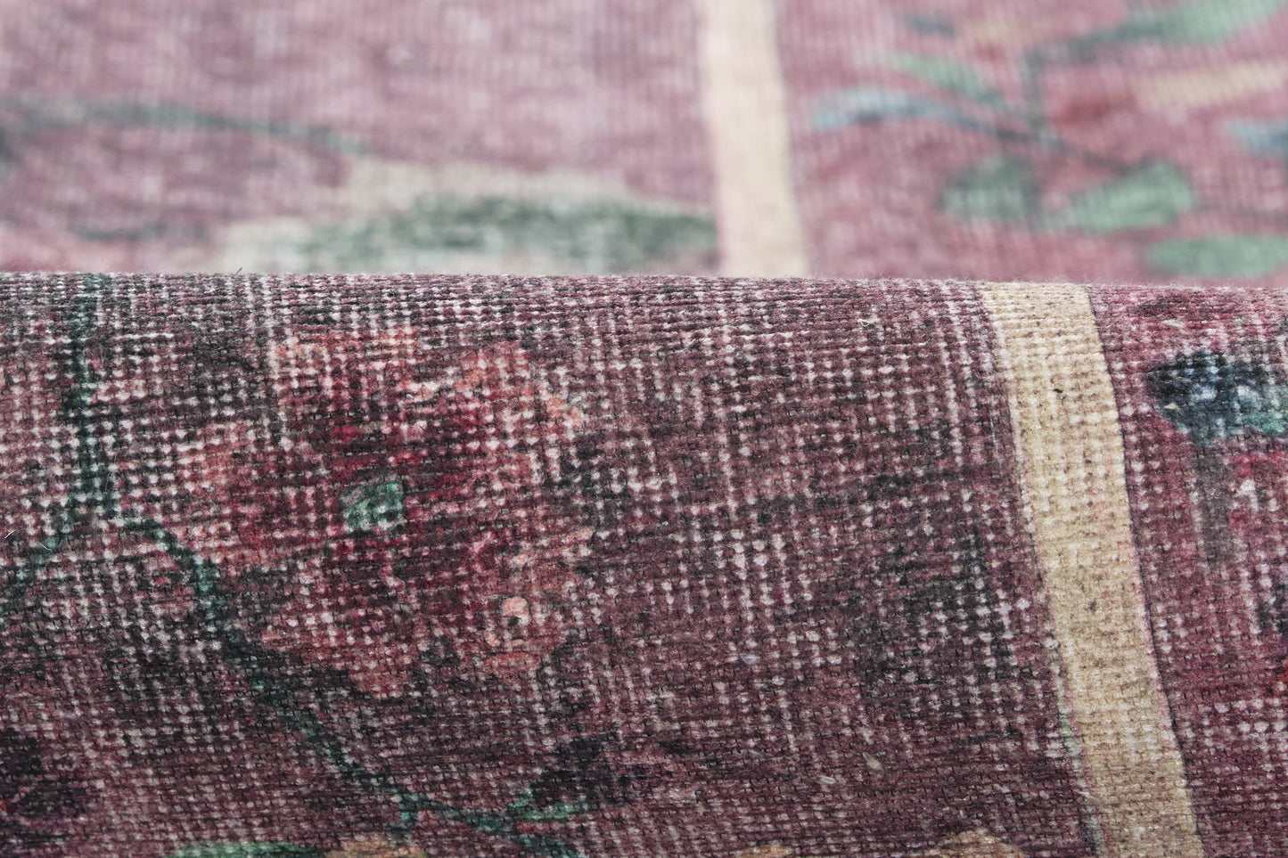 Close-up of a purple-maroon woven rug with cream and teal floral pattern; textured vintage textile.