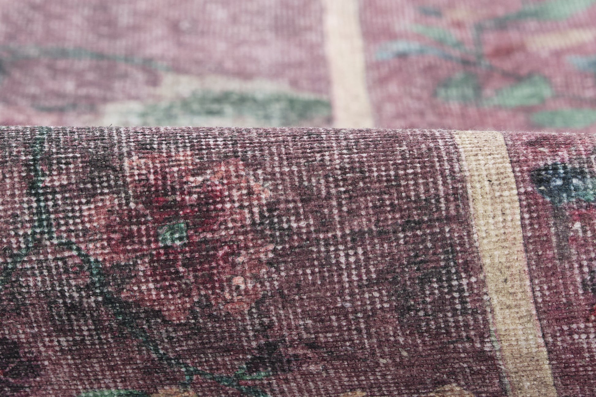 Close-up of a purple-maroon woven rug with cream and teal floral pattern; textured vintage textile.