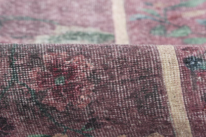 Close-up of a purple-maroon woven rug with cream and teal floral pattern; textured vintage textile.