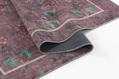 Purple rug with green floral motifs and a cream border; rolled edge showing grey backing.
