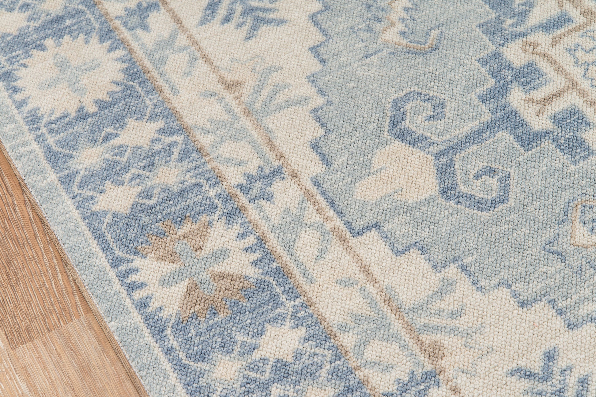 Blue and beige ornamental area rug with floral motifs on a wooden floor.