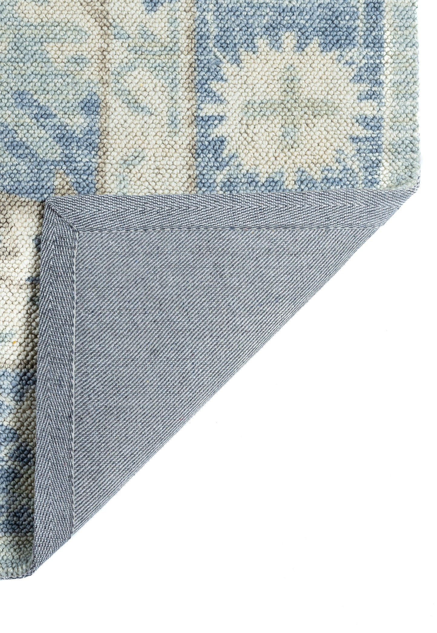 Blue woven area rug with cream sunburst medallion and floral border; folded corner reveals denim-blue backing.
