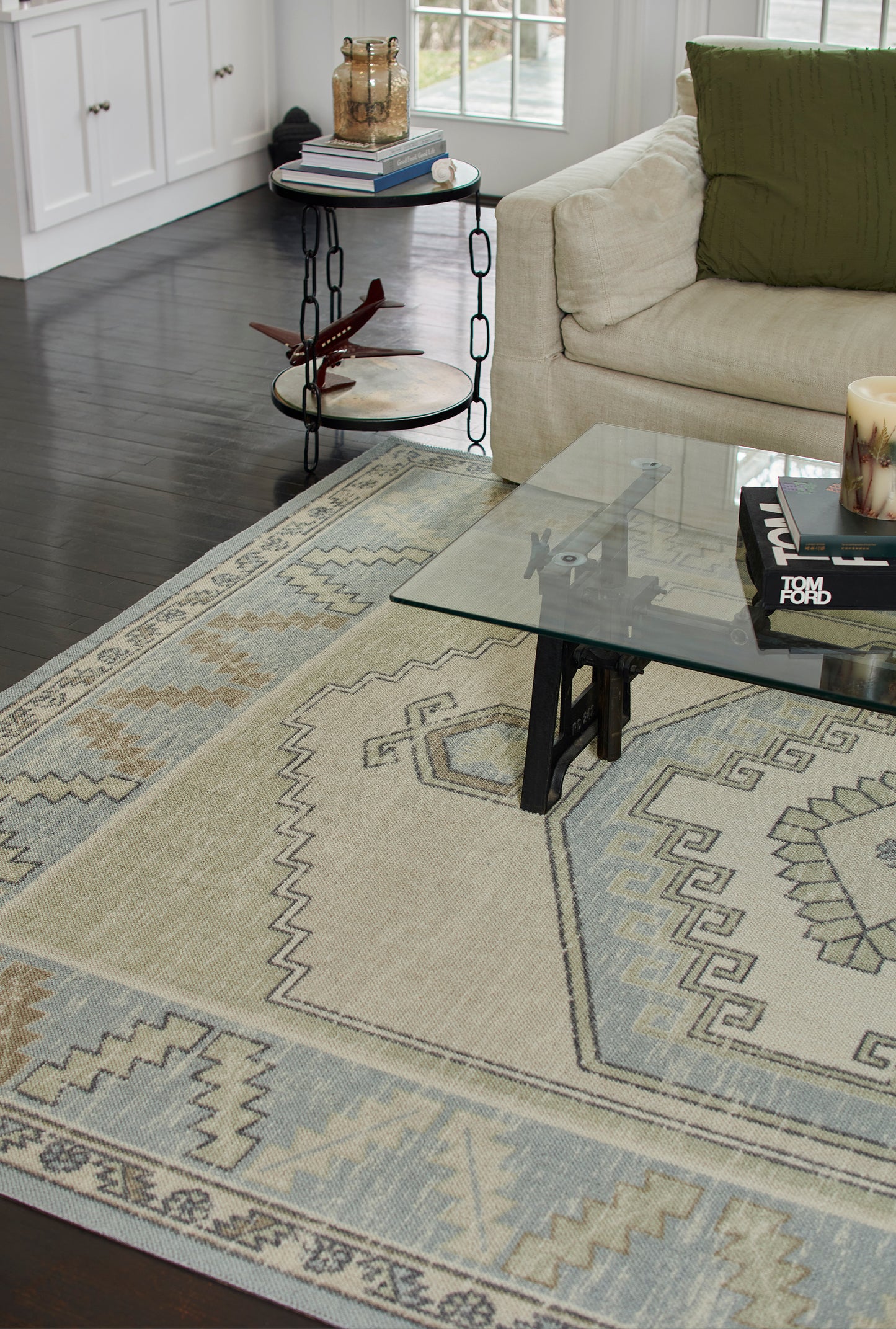 Geometric beige area rug with light blue and gray motifs under a glass coffee table in a modern living room.