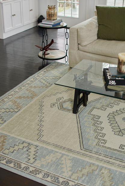 Geometric beige area rug with light blue and gray motifs under a glass coffee table in a modern living room.
