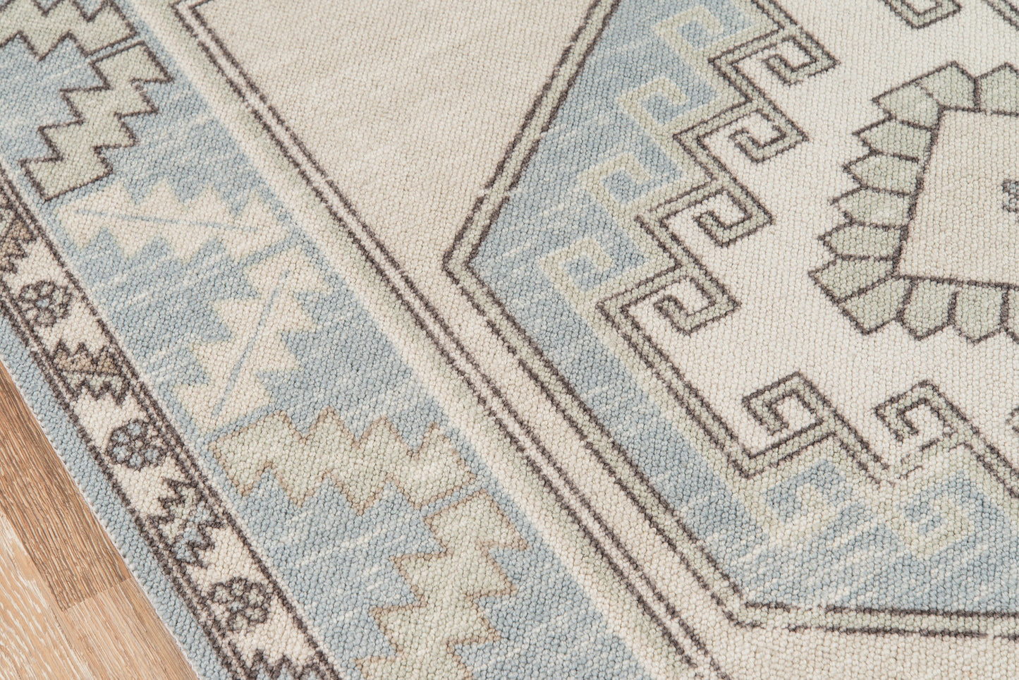 Light blue and beige geometric woven rug with tribal motifs on a wooden floor.
