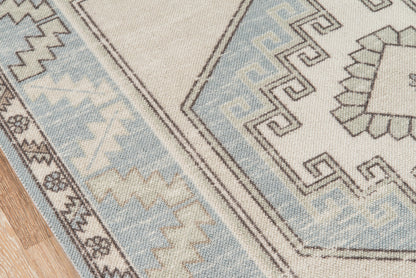 Light blue and beige geometric woven rug with tribal motifs on a wooden floor.