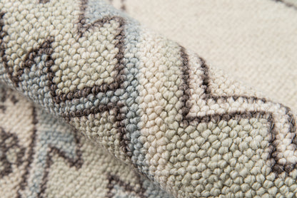 Close-up of a beige woven rug with geometric chevron pattern in brown and gray.