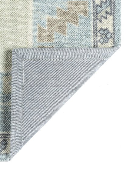 Pastel geometric rug in sky blue, ivory and beige; folded corner shows blue-grey underside and clean binding.