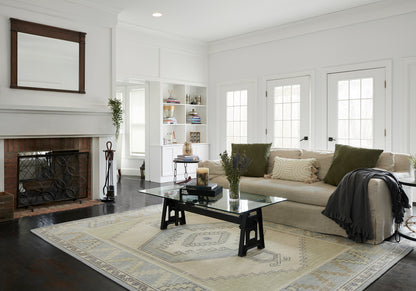 Bright contemporary living room with beige sofa, glass coffee table, patterned rug, white walls, fireplace, built-in shelves.