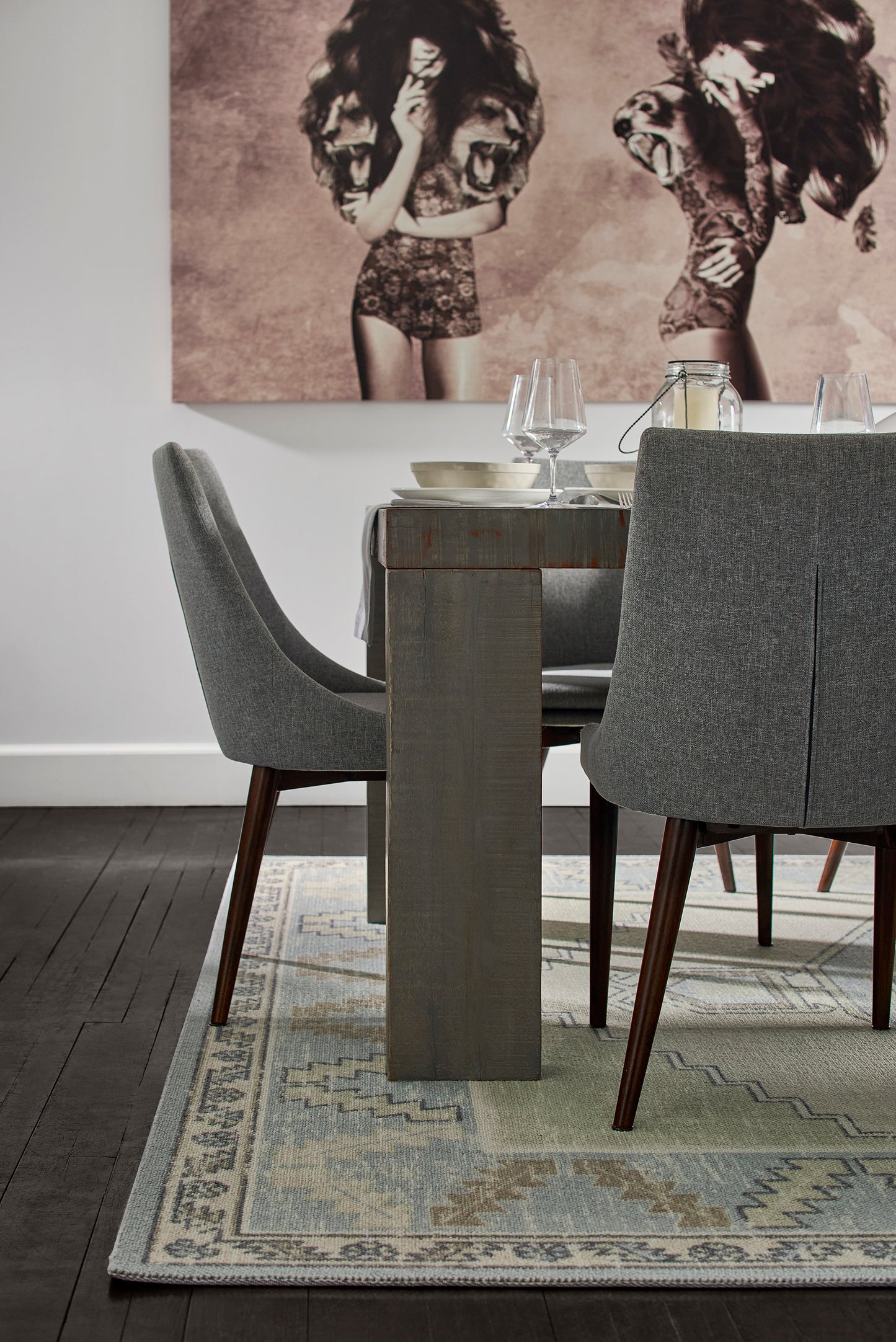 Gray upholstered dining chairs, block-style wood table leg, light-blue patterned rug, modern dining room setup.