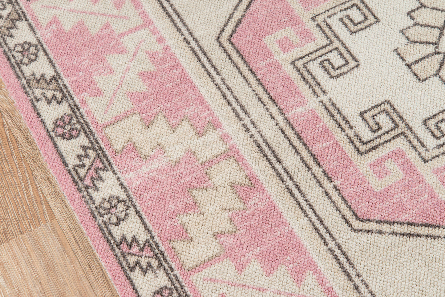 Pink and cream geometric rug with black outlines and tribal motifs on light wood floor.