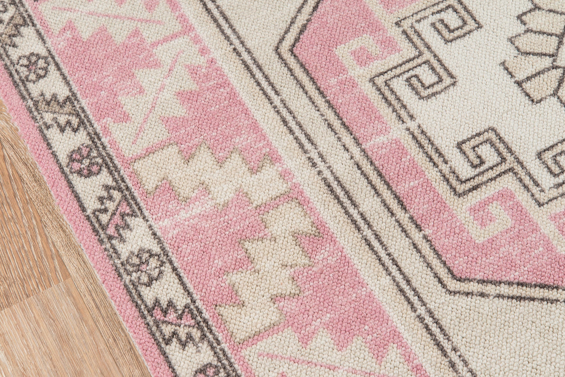 Pink and cream geometric rug with black outlines and tribal motifs on light wood floor.